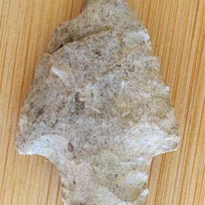 May include: A gray stone arrowhead with a pointed tip and a rough, textured surface.