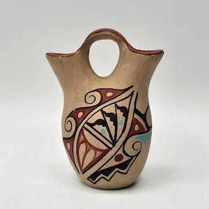 Pode incluir: Um pequeno vaso de cerâmica pintado à mão com um design tradicional do sudoeste. O vaso é marrom com detalhes em vermelho, preto e turquesa. Tem um design único de bico duplo e uma alça.
