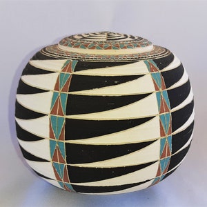 Puede incluir: Un jarrón de cerámica blanca con un patrón geométrico en blanco y negro. El jarrón tiene una tapa con un patrón similar. El jarrón está decorado con acentos rojos, azules y turquesa.