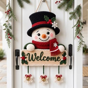 Puede incluir: Un adorno de pared de ganchillo con forma de muñeco de nieve, sombrero negro, bufanda roja y un letrero de madera con la palabra Welcome en verde. Tres copos de nieve de ganchillo blancos con cascabeles dorados cuelgan de la parte inferior.