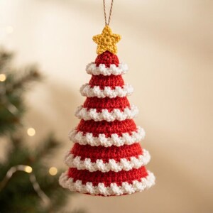 May include: A cone-shaped crochet Christmas tree ornament in red with white ruffled trim layers. The tree is topped with a small yellow crocheted star and features a thin brown string loop at the top for hanging, creating a festive decoration.