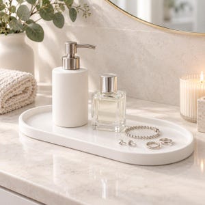 Peut inclure: Un plateau ovale blanc contient un distributeur de savon blanc avec une pompe argentée, un flacon de parfum en verre transparent avec un bouchon argenté, un bracelet en perles argentées, deux petites boucles d'oreilles et une bague.