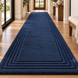 May include: A long, rectangular navy blue runner rug featuring a textured, tufted surface and a series of concentric, recessed rectangular borders that frame the center. The rug has a deep, solid blue color and a consistent, dense pile construction.
