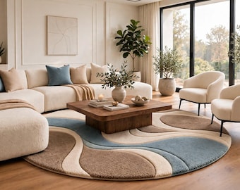 Puede incluir: Una alfombra circular grande con un patrón abstracto ondulado en tonos crema, beige y azul polvoriento. La alfombra tiene un pelo texturizado y afelpado, colocada sobre un suelo de madera bajo una mesa de centro cuadrada de madera.