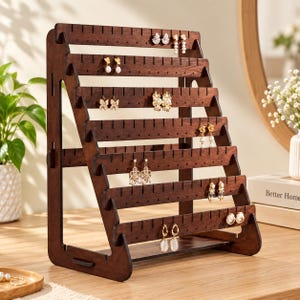 May include: A dark brown wooden earring display stand featuring six tiered horizontal bars with evenly spaced slots for hanging jewelry. The structure is supported by two side panels and includes a flat base, showcasing various pairs of earrings.