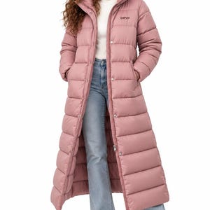 Peut inclure: Un long manteau doudoune rose poudré avec une capuche, une fermeture éclair frontale avec boutons-pression et le texte "DRYP" imprimé en noir sur la poitrine gauche. Le manteau est porté sur un pull à col roulé blanc, un jean bleu clair et des baskets blanches.
