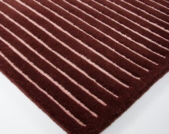 May include: A rectangular rug featuring a deep burgundy background with a series of parallel, vertical light pink stripes. The surface has a textured, tufted appearance with consistent spacing between the lines across the entire fabric.