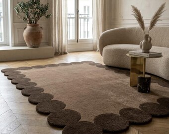 May include: A rectangular area rug featuring a light brown center and a dark brown border composed of a continuous scalloped edge of circular shapes. The rug has a thick, textured pile and is positioned on a light-colored wooden floor.