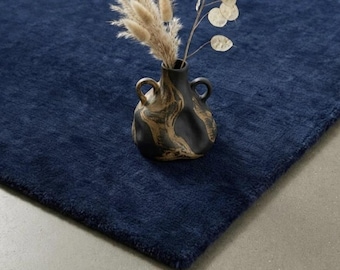 May include: A deep navy blue area rug with a plush, textured surface. Resting on the rug is a black ceramic vase with two handles and a swirling tan marbled pattern, containing dried beige pampas grass and silver dollar eucalyptus stems.