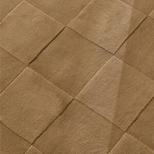 Close-up of a toffee brown hand tufted rug showcasing its raised geometric checkerboard pattern, textured pile, and subtle high low surface details.