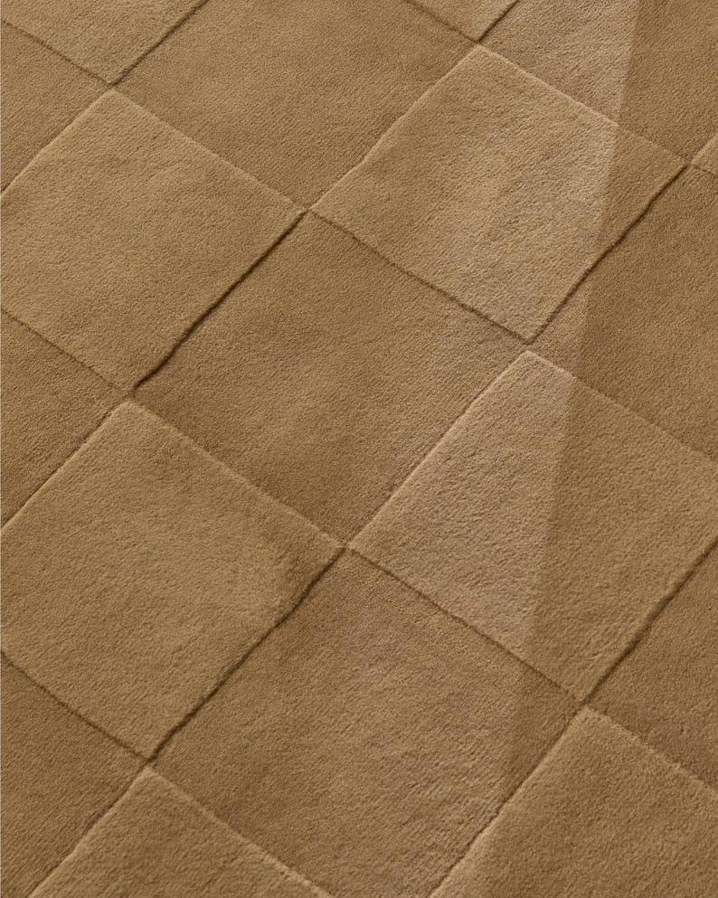 Close-up of a toffee brown hand tufted rug showcasing its raised geometric checkerboard pattern, textured pile, and subtle high low surface details.