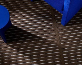 May include: A rectangular area rug featuring a dark brown base with thin, horizontal white stripes. The rug is positioned beneath a bright blue armchair and a matching blue side table, creating a contrast between the dark and vibrant colors.