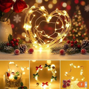 May include: A collection of decorative LED string lights featuring flexible copper wire shaped into a heart, a circle with red and green bows and small bells, and a star. The lights emit a warm glow and are accented by pine branches and berries.