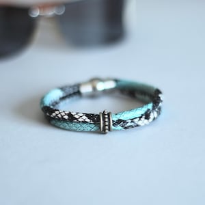 May include: A blue and black braided bracelet with a silver clasp and a silver bead accent.