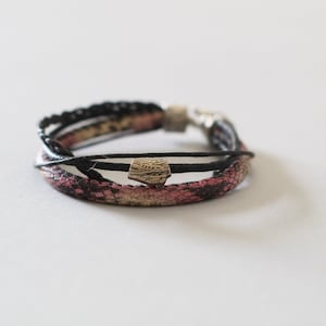 May include: A multi-strand bracelet with a pink and black snakeskin pattern and a silver charm.
