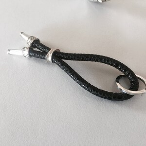 Peut inclure: Un porte-clés en cuir noir avec des accents argentés et un anneau argenté.
