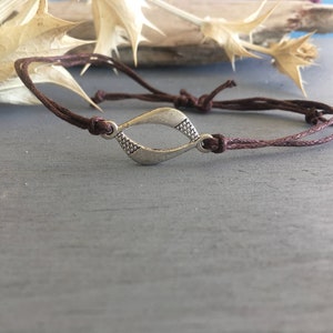 May include: A brown cord bracelet with a silver, open, teardrop-shaped charm.