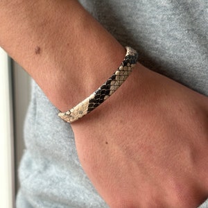 May include: A black and white snakeskin bracelet on a person's wrist.