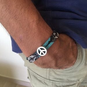 Puede incluir: Un brazalete de cuerda trenzada negro y turquesa con un dije de plata con el signo de la paz.
