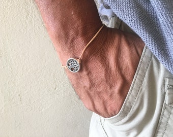 May include: A tan leather cord bracelet with a silver tree of life charm.