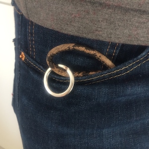 Könnte beinhalten: Ein silberner Schlüsselring mit einer braunen Lederschlaufe. Der Schlüsselring hängt an einer blauen Jeans-Tasche.