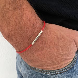 Puede incluir: Un brazalete de cuero rojo con un acento de barra de plata.