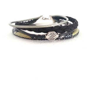 Pode incluir: Um bracelete em camadas com couro trançado preto, um fecho de metal prateado e uma tira de couro com padrão verde e preto.