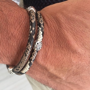 Peut inclure: Un bracelet double tour en cuir d' serpent noir et blanc avec des accents argentés. Le bracelet a un motif de tête de serpent avec des yeux argentés.