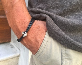 Puede incluir: Un brazalete de cuero negro con un dije de ancla de plata.