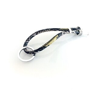 Może przedstawiać: Brelok do kluczy z czarno-złotym wzorem i srebrnym kółkiem.