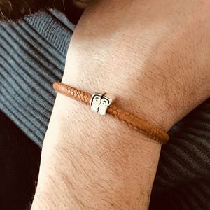 May include: A brown leather bracelet with a silver charm featuring a couple kissing.