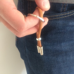 May include: A brown leather keychain with silver metal accents. The keychain is attached to a loop of leather and has two silver metal rings.