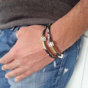 Puede incluir: Una pulsera trenzada negra y amarilla con dijes de dados plateados.