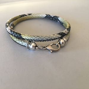 Puede incluir: Un collar de cordón trenzado negro, blanco y verde con cierres de metal plateado.