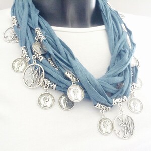 Op de afbeelding: Een blauwe stoffen ketting met zilveren boom- en muntcharms. De ketting is gelaagd en heeft een bohemian stijl.