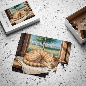 May include: A jigsaw puzzle featuring an orange tabby cat sleeping on a white cloth on a wooden windowsill. The scene shows a green lawn and a white fence through the window. The puzzle box is visible with the text Custom Made.