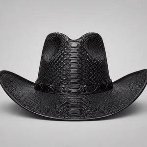 Puede incluir: Un sombrero de vaquero negro con un patrón texturizado de piel de serpiente en la copa y el ala. El sombrero incluye una banda de piel de serpiente negra a juego que rodea la base de la copa, con una parte superior pellizcada y ala curva.