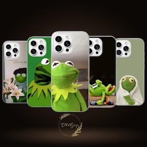 May include: Five smartphone cases featuring various images of a green frog puppet. The designs include the frog with flowers, a graphic illustration, a close-up portrait, the frog lying down with bottles, and the frog wrapped in a white towel.