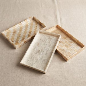 May include: Three rectangular trays with raised edges, each featuring a distinct mosaic pattern. One tray displays a chevron design in shades of tan and cream, while the other two feature varied rectangular tile patterns in white and beige tones.