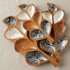 Può includere: Un set di due piatti da portata in legno a forma di foglia con sezioni intarsiate in madreperla bianca iridescente e conchiglia di abalone scura e screpolata. La venatura naturale del legno è visibile nelle forme organiche intagliate.