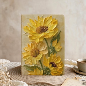 May include: A rectangular notebook featuring a textured, three-dimensional impasto painting of bright yellow sunflowers with dark brown centers and green leaves on a cream-colored background. The cover displays thick, visible brushstrokes.