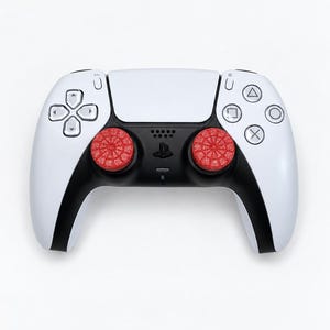 May include: A white and black video game controller featuring two textured, circular red thumbstick covers. The controller includes a central touchpad, a directional pad on the left, and four action buttons on the right with triangle, circle, cross, and square symbols.