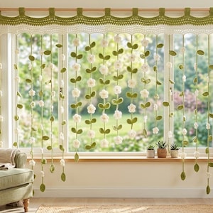 May include: A decorative window valance and hanging curtain set featuring a crocheted olive green and cream top border with multiple vertical strands of crocheted green leaves and small white flowers suspended from the valance across the window.