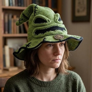 May include: A lime green crocheted hat featuring a pointed, slouchy top with black stitched details, a wide brim, and a prominent black facial expression with large eyes and a mouth. A circular brown emblem is attached to the front of the brim.