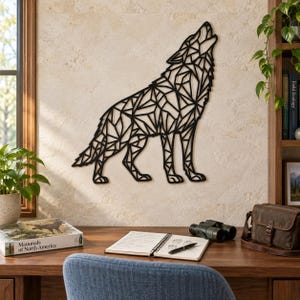 Op de afbeelding: Een zwart geometrisch wandkunstobject in de vorm van een huilende wolf, bestaande uit een complex netwerk van onderling verbonden lijnen en driehoeken. Het ontwerp is bevestigd aan een lichte stenen muur en toont een scherp, hoekig silhouet.