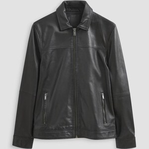 Puede incluir: Una chaqueta de cuero negra con cuello clásico, cierre de cremallera frontal completo y dos bolsillos verticales con cremallera en la parte inferior. La chaqueta tiene mangas largas con puños y un acabado negro liso y uniforme.