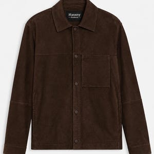 Puede incluir: Una chaqueta de ante marrón oscuro con cuello clásico, cierre frontal de botones a juego y un bolsillo en el pecho en el lado izquierdo. La etiqueta interior del cuello muestra el texto Hassny Products en letras de color blanco.