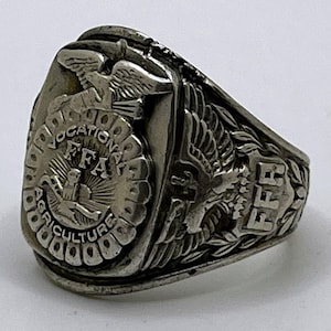 May include: Silver-toned ring with the letters "FFA" prominently displayed. The ring features an eagle emblem and the words "Vocational Agriculture". The ring has a detailed design and a classic style.