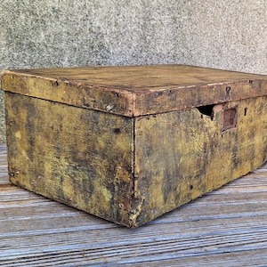 May include: A vintage wooden box with a hinged lid, painted in a faded yellow and green color. The box has a worn and rustic appearance, with visible signs of age and use.
