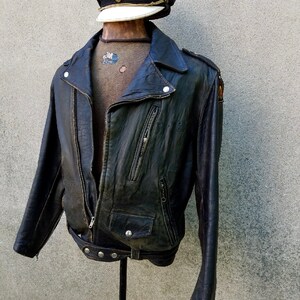 May include: A black leather biker jacket with a zip fastening and a belt. The jacket has a distressed look and features a patch on the left sleeve.